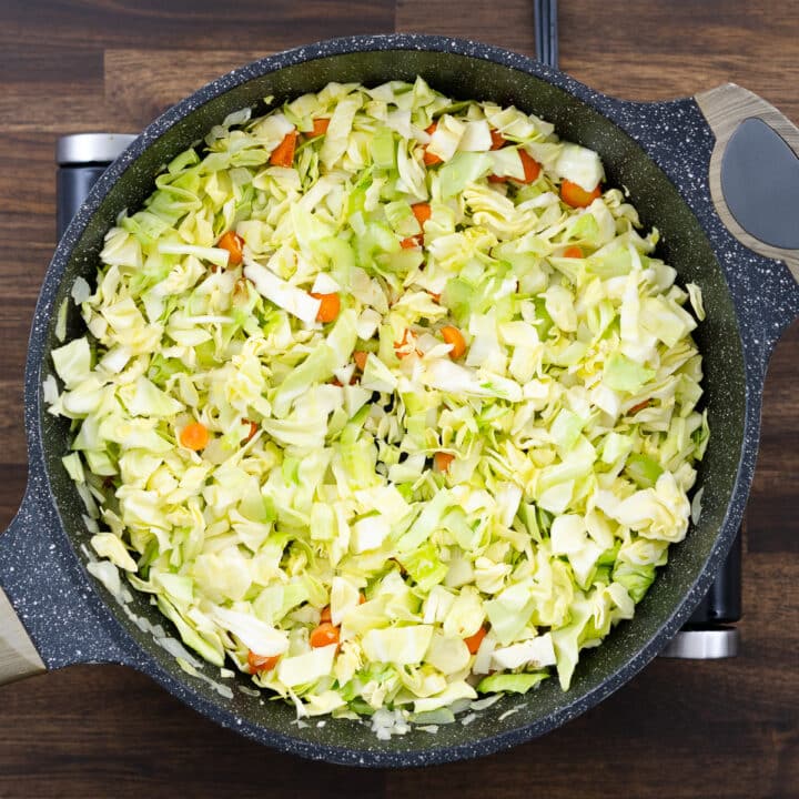 A pan with cabbage sautéed along with veggies and aromatics.
