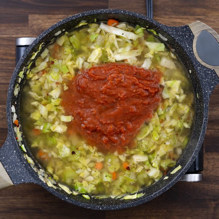 A pan with veggies, cabbage, crushed tomatoes and broth.
