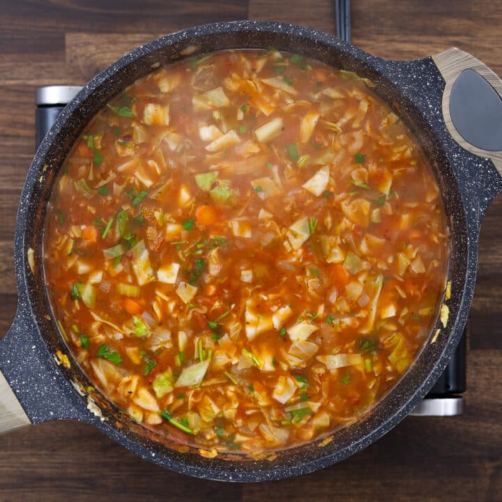 A pan with cabbage soup garnished with fresh parsley leaves.