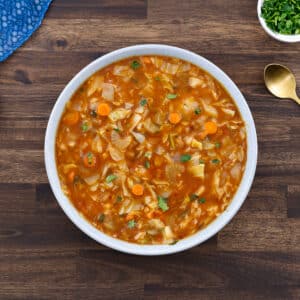 Cabbage soup served in a white bowl with fresh parsley on the side.