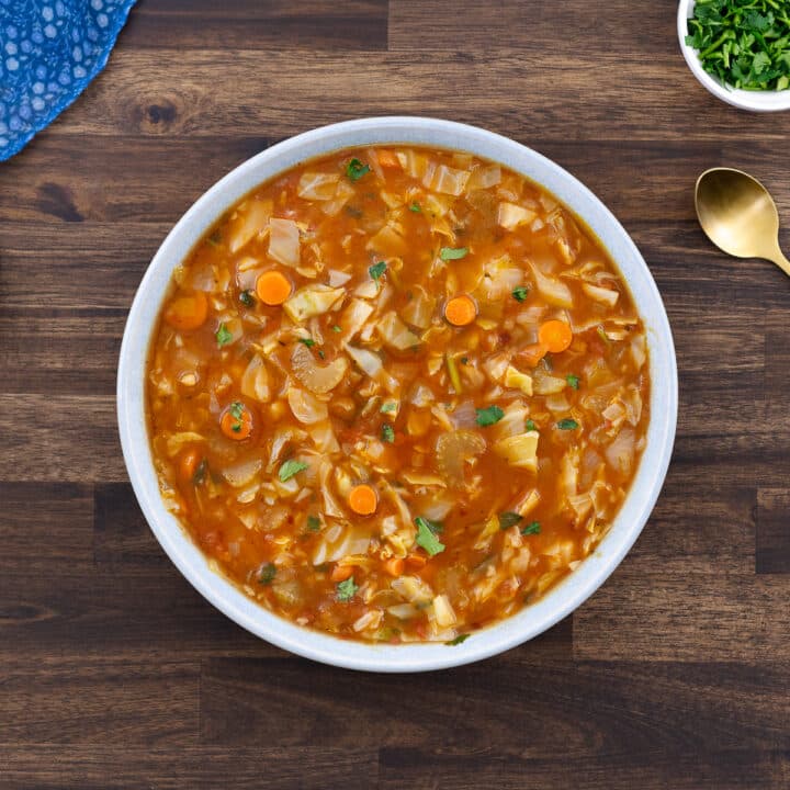 Cabbage soup served in a white bowl with fresh parsley on the side.