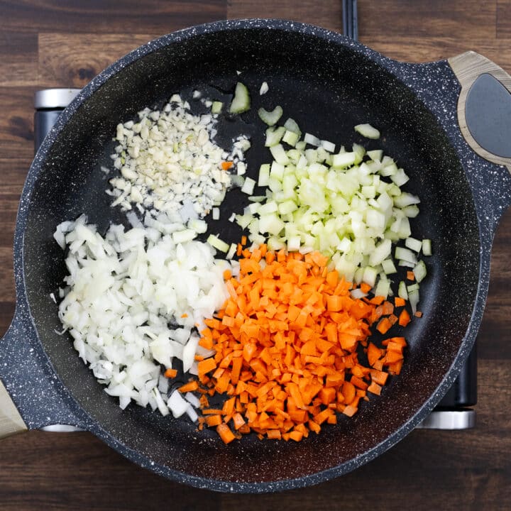 A pan filled with chopped aromatics and vegetables, ready to be sautéed.