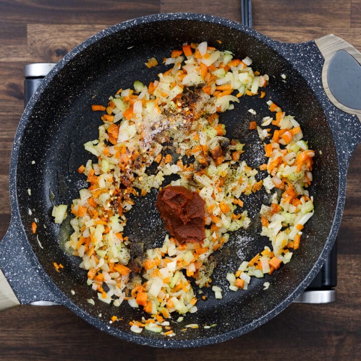 A pan with sautéed aromatics and vegetables, seasoned with spices and Italian seasoning.
