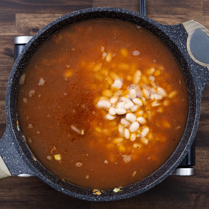 A pan with aromatics, vegetables, and beans mixed into tomato sauce and broth.