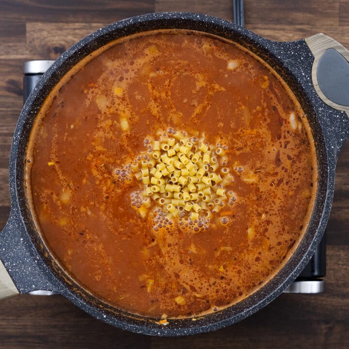 A pan with a hearty mixture of vegetables, beans, and broth, with pasta added in.