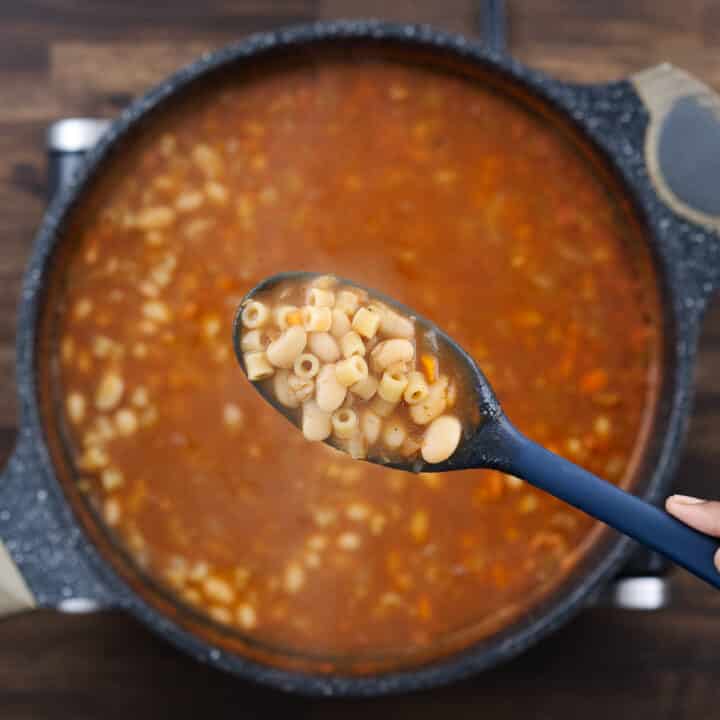 A close-up of a blue spoon showing the cooked texture of pasta and beans.