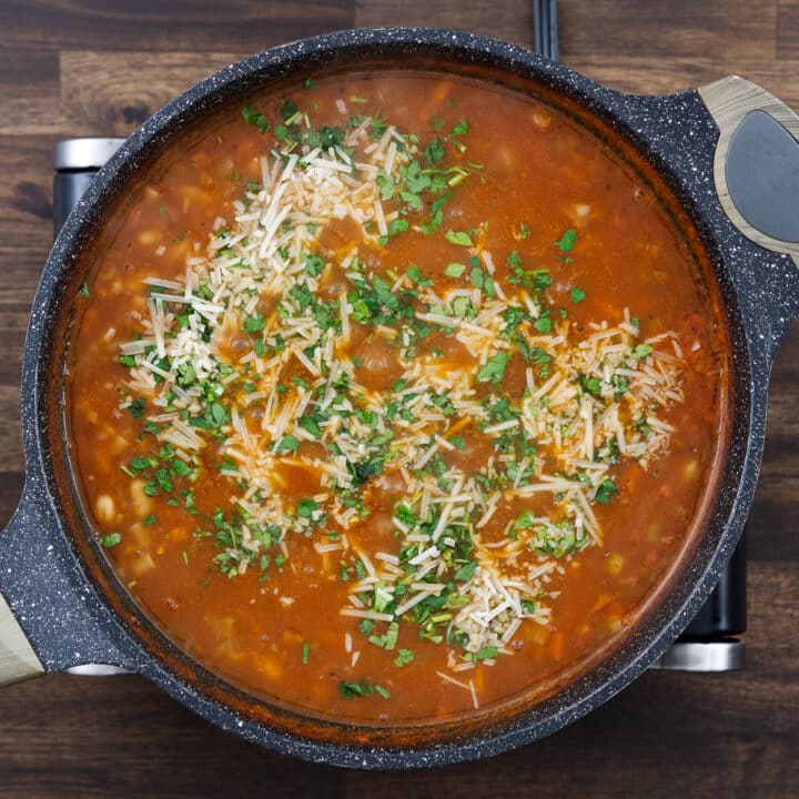 A pan of pasta e fagioli, garnished with freshly grated Parmesan cheese and chopped parsley.