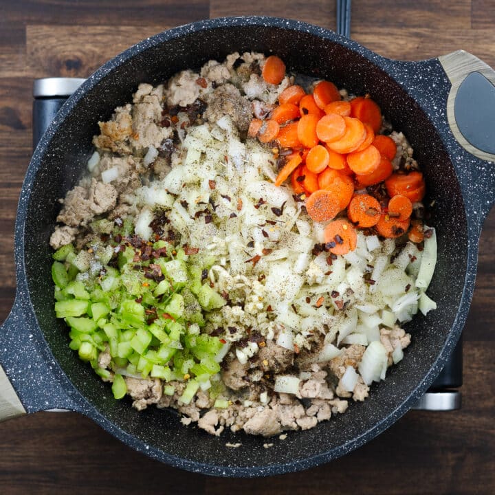 Pan with cooked ground meat, veggies, and seasoned with seasoning powders.