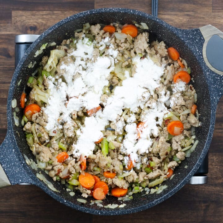 Pan with cooked ground meat and sautéed veggies sprinkled with all-purpose flour.