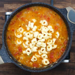 Pan with soup mixture of ground meat, veggies, and tortellini pasta.