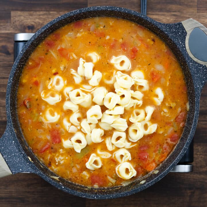 Pan with soup mixture of ground meat, veggies, and tortellini pasta.