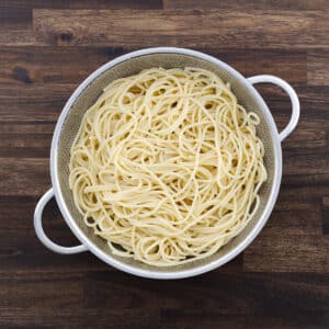 A colander with cooked pasta, ready to be tossed in garlic-infused oil.