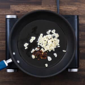 A pan with garlic cloves and chili flakes sizzling in olive oil.