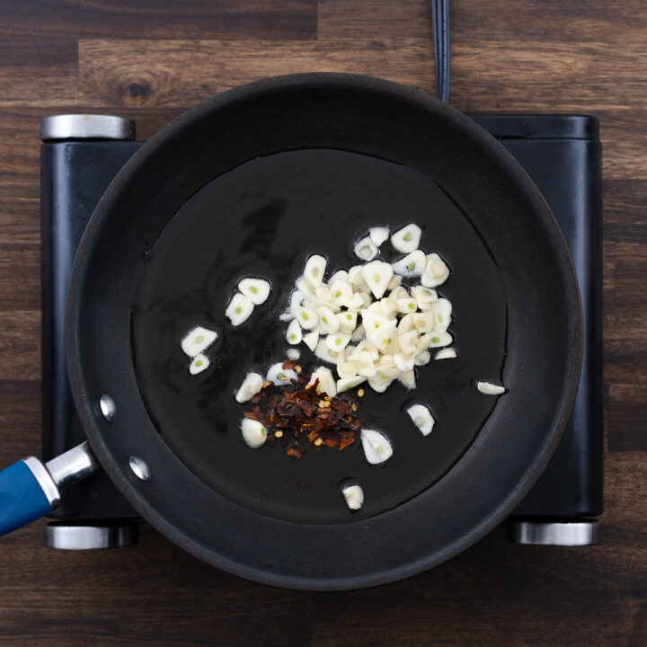 A pan with garlic cloves and chili flakes sizzling in olive oil.