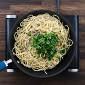 A pan with cooled spaghetti, seasoned with black pepper, salt, parsley, and tossed in garlic-infused olive oil.