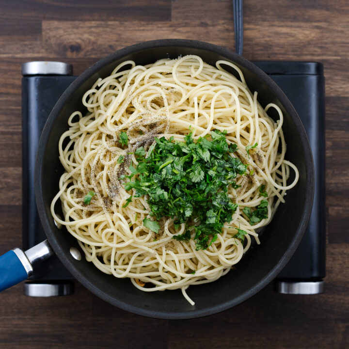 A pan with cooled spaghetti, seasoned with black pepper, salt, parsley, and tossed in garlic-infused olive oil.