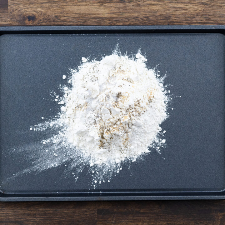 A tray filled with all-purpose flour seasoned with black pepper, salt, and garlic powder.