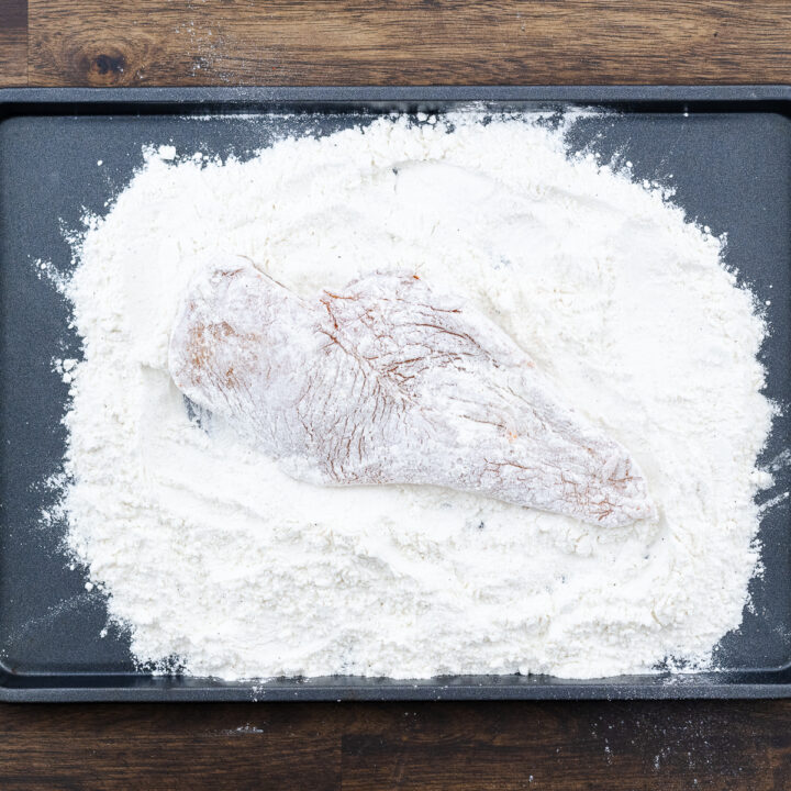 A boneless chicken breast coated in the seasoned flour mixture.