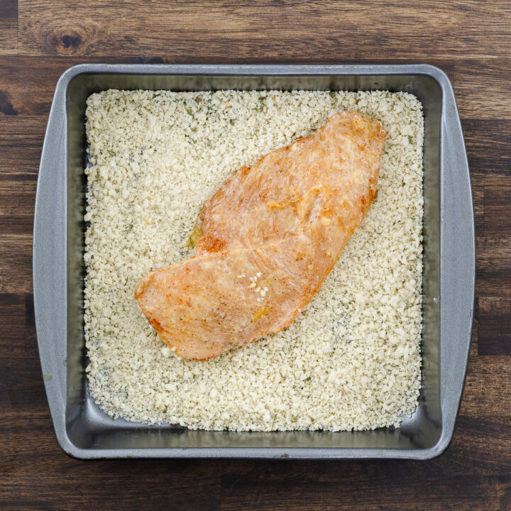 Egg-coated chicken breast being covered in a panko breadcrumb mixture.