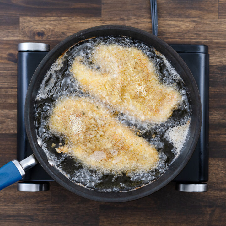 A breaded chicken breast frying in hot oil in a pan.