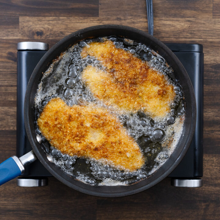 A pan with golden brown fried chicken schnitzel in oil.