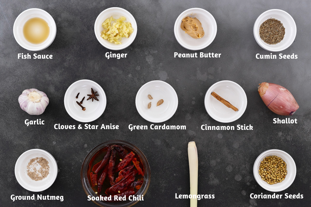 Thai Massaman Curry ingredients on a gray table: fish sauce, ginger, peanut butter, cumin seeds, garlic, cloves, star anise, and more.