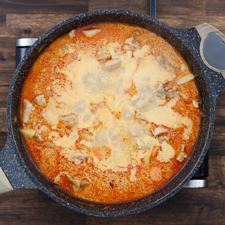 A pan with simmering curry with chicken and veggies.