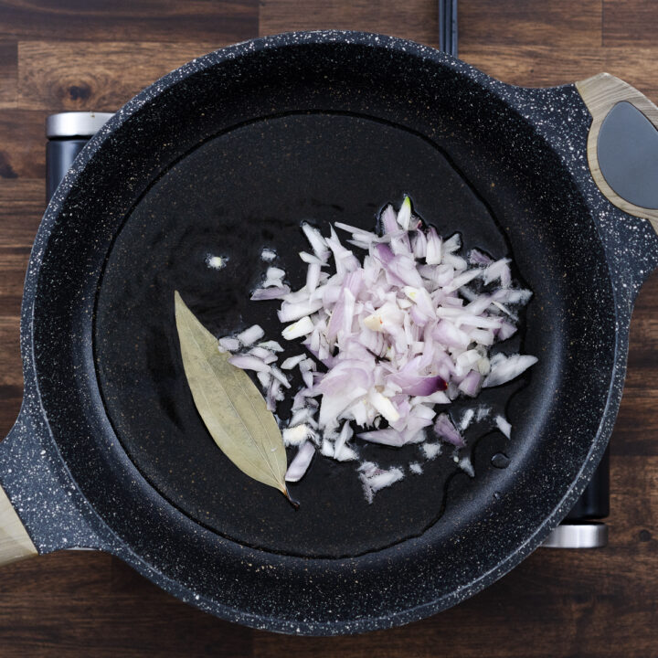 Pan with bay leaf and shallots sautéing in oil.