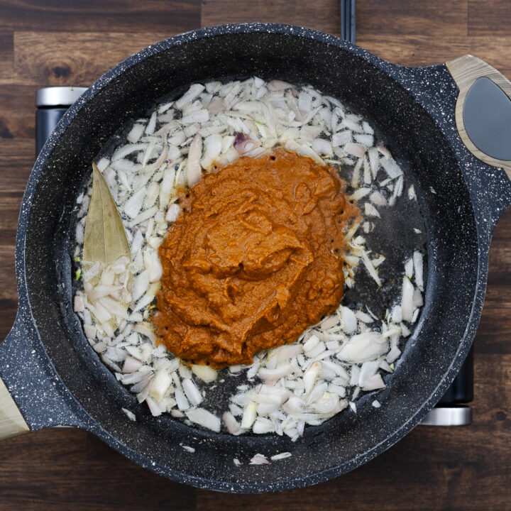 Sautéed shallots mixed with curry paste in a pan.