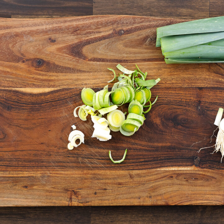 Chopped white and light green parts of leeks on a wooden cutting board, ready for cooking.