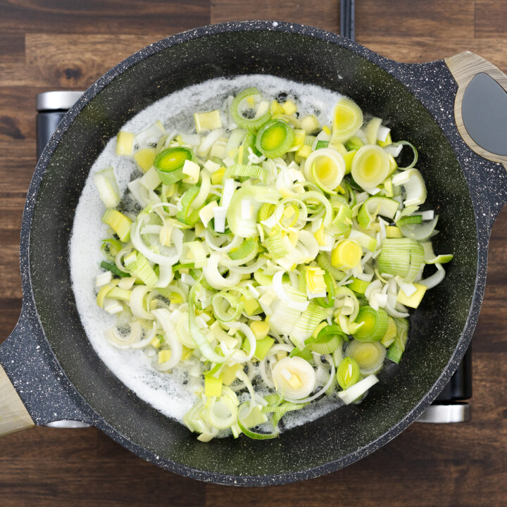 A pan with freshly chopped leeks sautéing in melted butter, turning soft and fragrant.