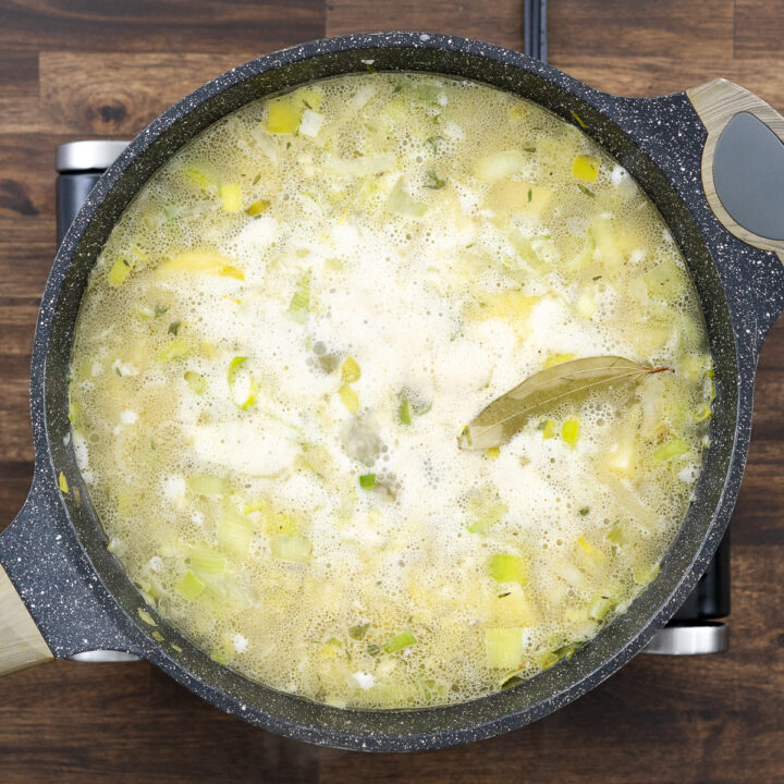 A pan with a simmering mixture of potatoes and leeks in a flavorful broth.