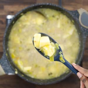 A close-up of a blue spatula lifting tender, fully cooked potatoes from the soup.