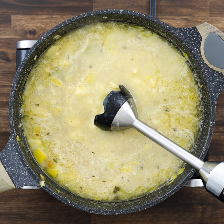 A pan with a potato and leek mixture in broth, ready for blending with an immersion blender.