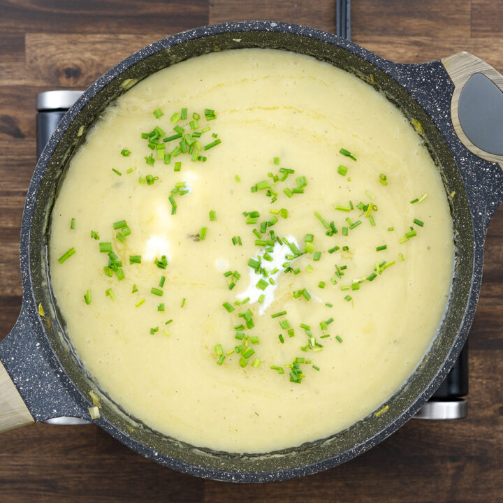 A creamy potato leek soup in a pan with milk and freshly chopped chives stirred in.