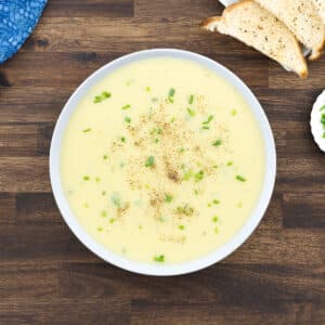 A white bowl of potato leek soup, garnished with chives and freshly ground black pepper.