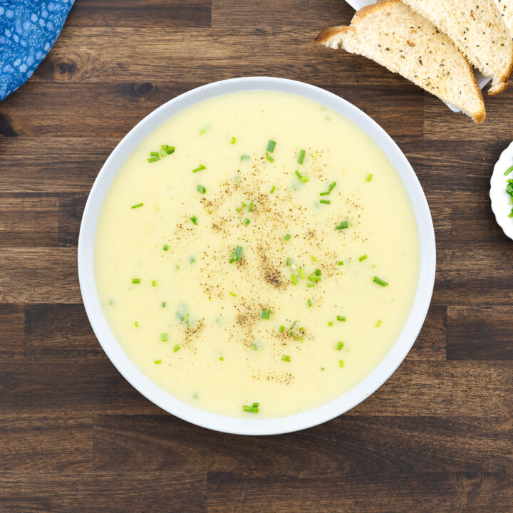 A white bowl of potato leek soup, garnished with chives and freshly ground black pepper.