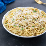 A white cup of Cacio e Pepe on a gray table, with a golden fork, and a blue towel nearby.