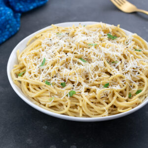 A white cup of Cacio e Pepe on a gray table, with a golden fork, and a blue towel nearby.