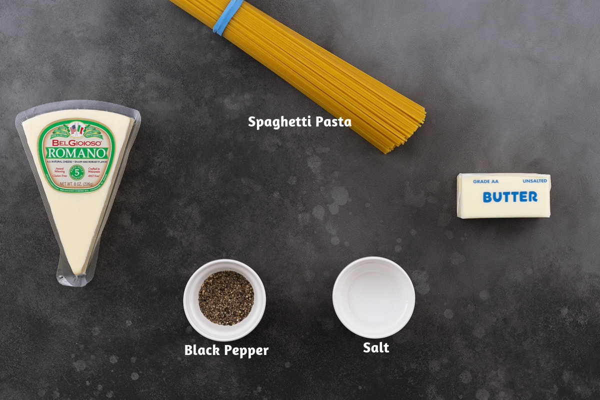 Ingredients for Cacio e Pepe on a gray table: Pecorino Romano cheese, spaghetti pasta, black pepper, and salt.