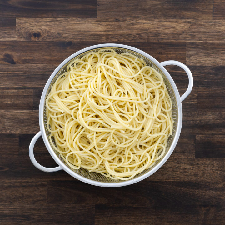 A colander with drained cooked spaghetti pasta.