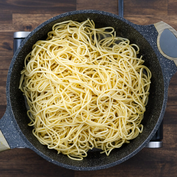 A pan with cooked pasta mixed into the pasta cooking water, butter, and black pepper mixture.