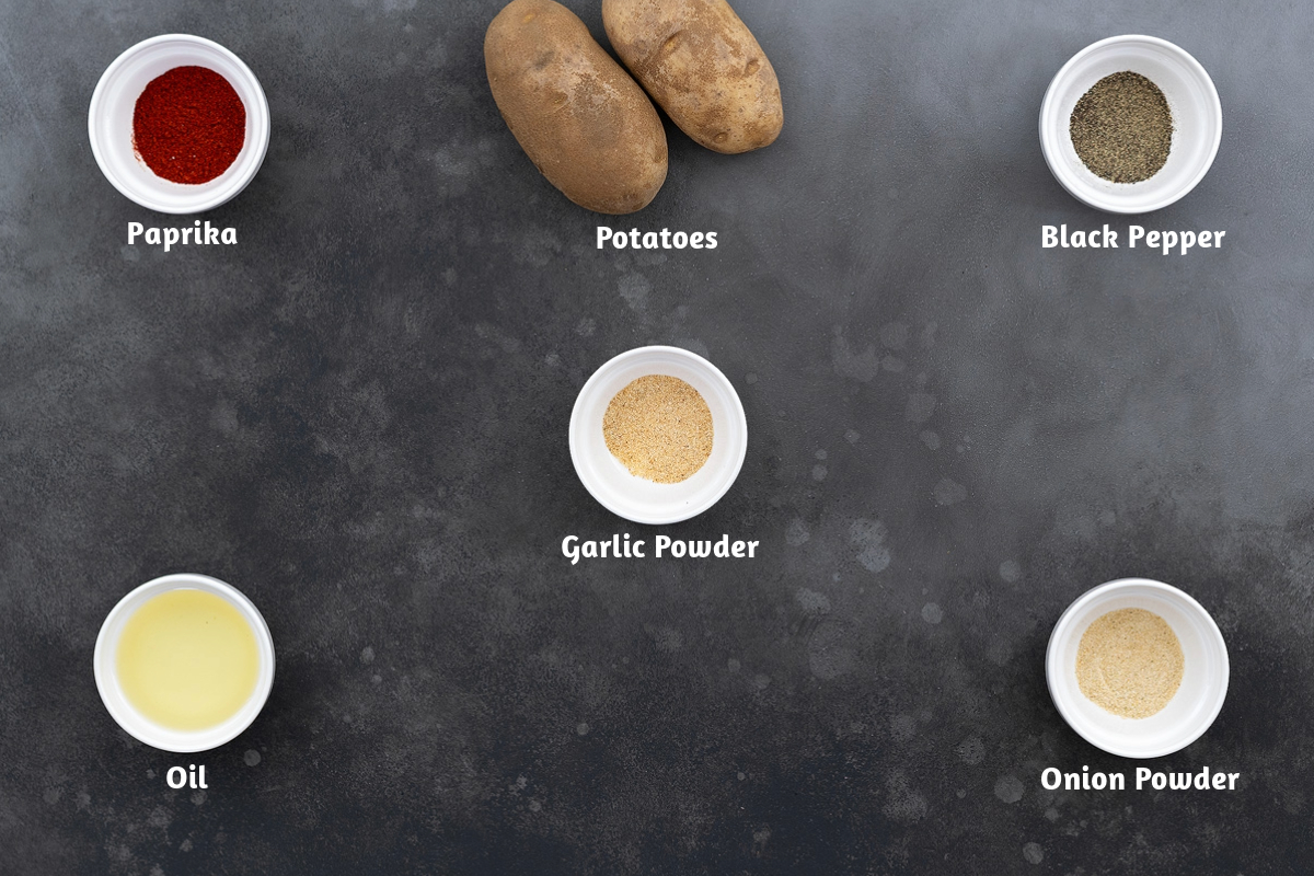 Fried potatoes ingredients placed on a gray table, including paprika, potatoes, black pepper, garlic powder, oil, and onion powder.