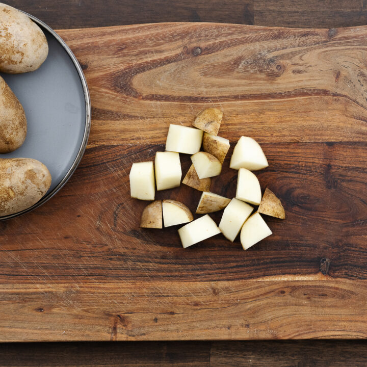 Wooden cutting board with diced potatoes.