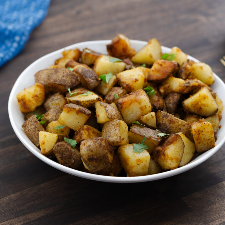 Fried potatoes served in a white bowl garnished with coriander leaves.
