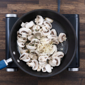 Sliced mushrooms, minced garlic, thyme leaves, black pepper, and salt added to the pan.