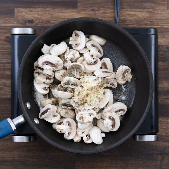 Sliced mushrooms, minced garlic, thyme leaves, black pepper, and salt added to the pan.