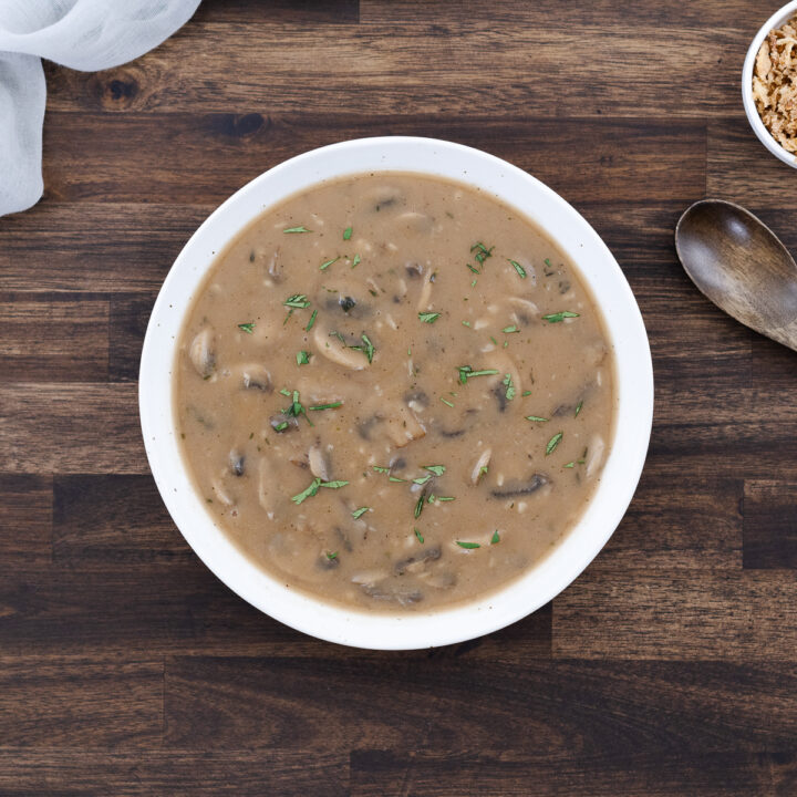 Mushroom gravy served in a white bowl with crispy fried onions on the side.