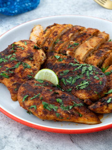 Pan-seared chicken breast with sliced pieces arranged on a plate, surrounded by a blue towel, a and golden fork.