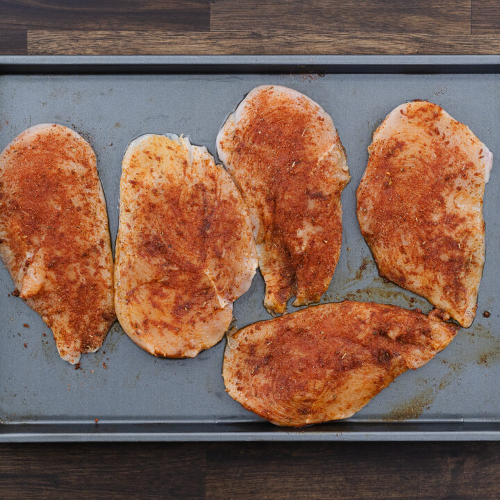 The chicken breast on a tray, evenly coated with the prepared seasoning mix.